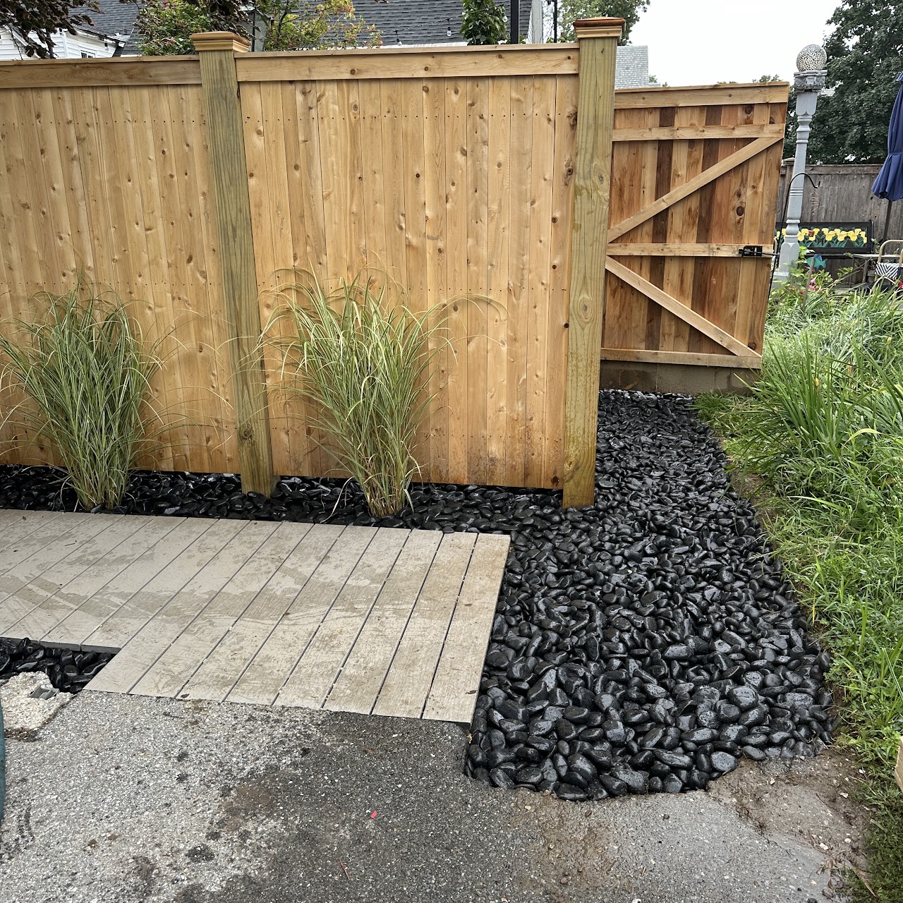 Black stone rock work and ornamental grasses along a fence line
